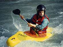 Photo of man in kayak holding paddle nearly parallel to the boat, surrounded by white water