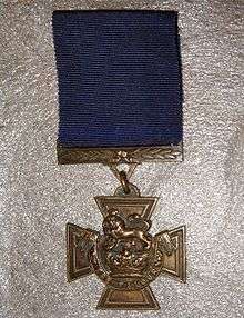 The obverse of the bronze cross pattée medal; showing the crown of Saint Edward surmounted by a lion with the inscription FOR VALOUR with a blue ribbon