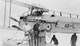 Large biplane on floats with three men in civilian clothes in the foreground