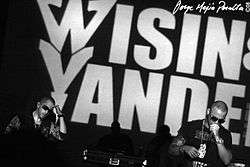 Two young men performing in front of large "Wisin & Yandel" background
