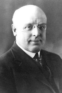 A bald, heavyset white man wearing round-rimmed glasses.