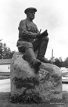 Sculpture of the writer Väinö Kataja seated on a rock, poised with a pen in his hand and a notebook on his knee