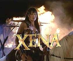 A woman in leather armor sits on horse back with flames behind her. At the bottom of the screen in capital letters is the word "Xena" in gold lettering.