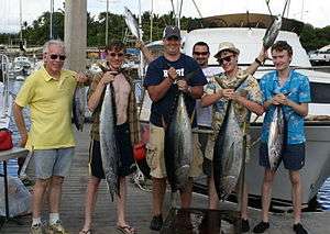 Photo of 6 men, four of whom are holding up tuna