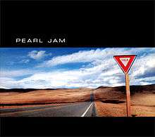 A triangular yield sign alongside a desertic road. Above and below the image are black bars, the top one having the text "Pearl Jam".