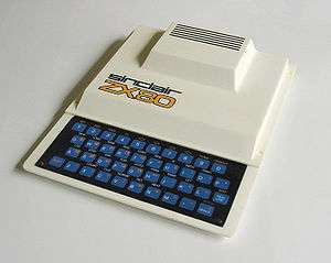 View of the ZX80, a white rectangular computer with a black keyboard with blue keys and the words "SINCLAIR ZX80" on the centre left of the case, in front of a large bulge at the rear of the machine.