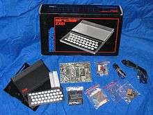The component parts of the ZX81, including the case, keyboard and circuitry, resting on a blue sheet in front of the cardboard box in which it was shipped.