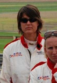 A female Australian cricketer in a tracksuit, wearing sunglasses, standing behind another woman in a tracksuit with sunglasses on the top of her head